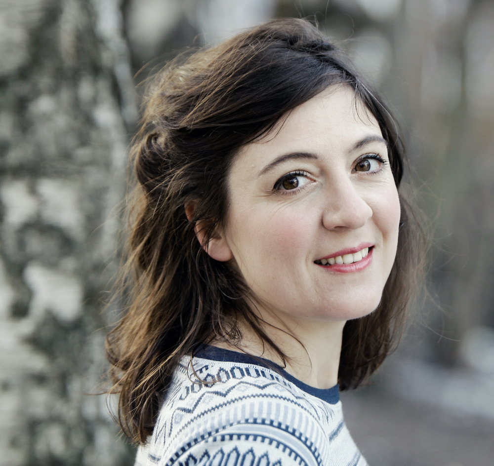 Portrait of Lorelou Desjardins smiling, wearing a patterned sweater, with a blurred natural background.
